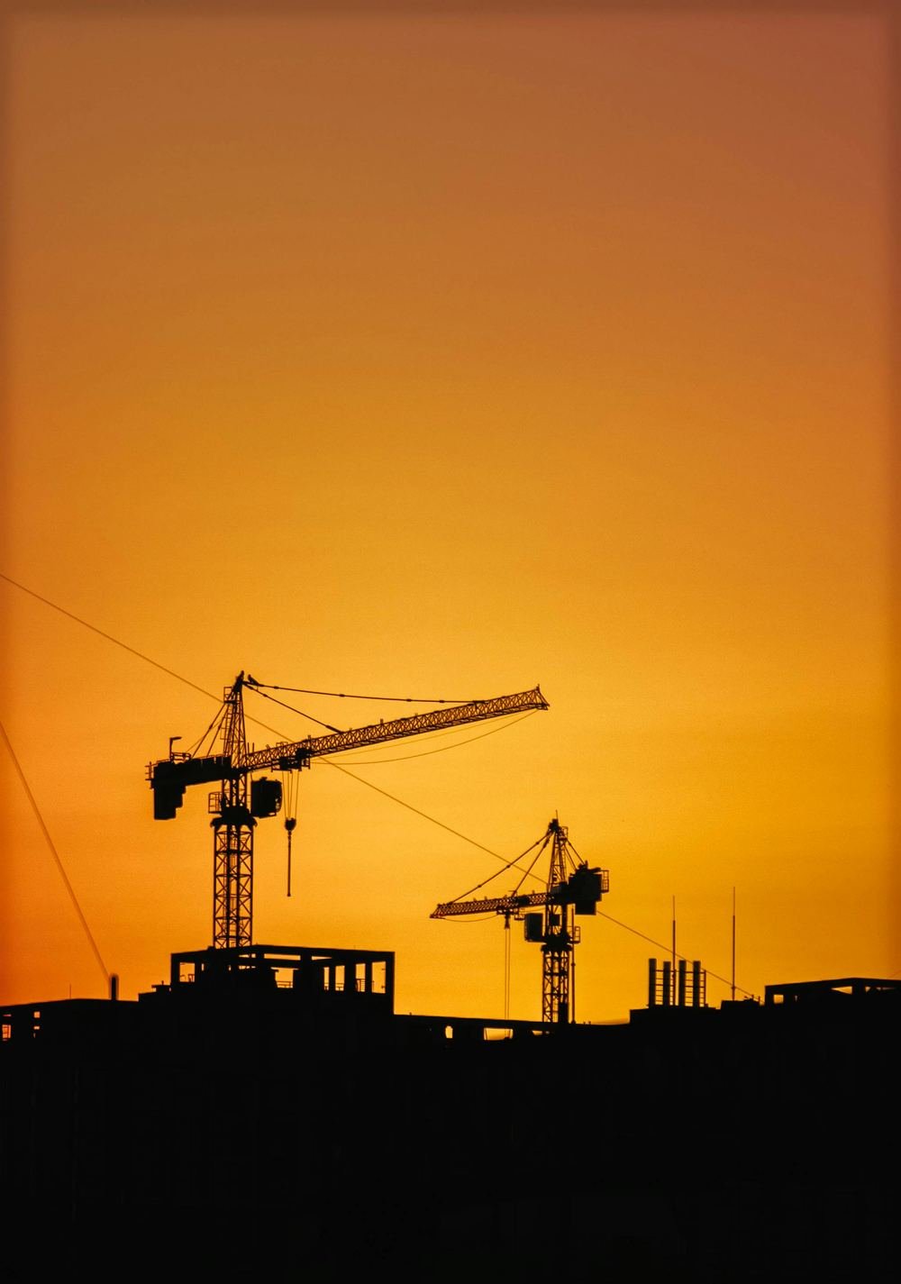 Construction cranes against an orange evening sky